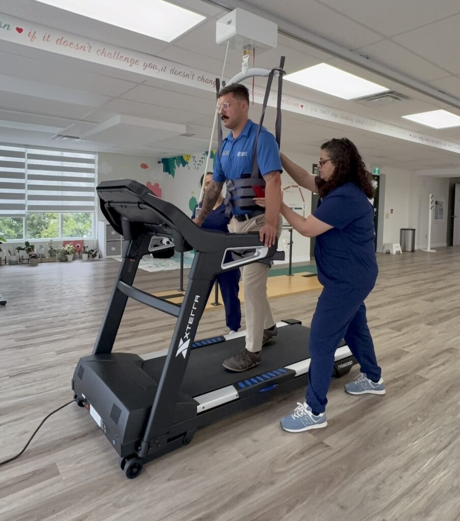 Physiotherapist guiding a patient through body weight assisted gait training on a treadmill with the Guldmann ceiling lift at Westwood in Guelph